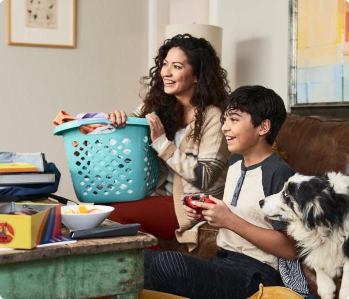 Woman holding laundry basket while son plays video game